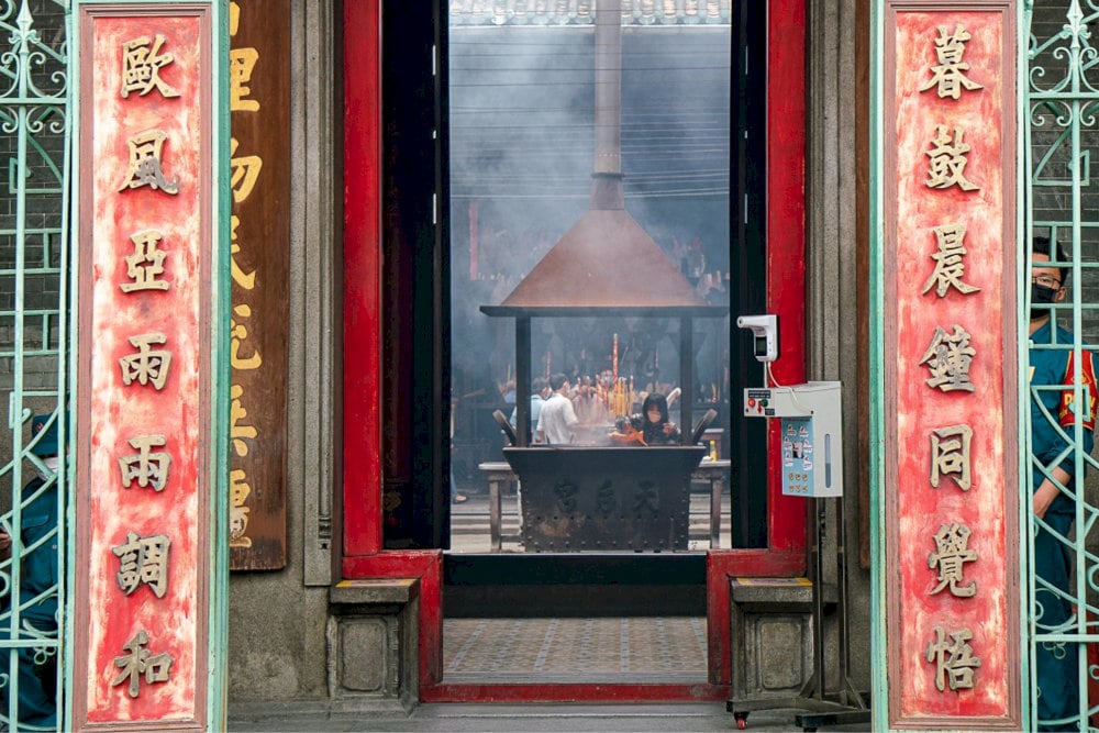 Close-up of intricately carved wooden gates, with red panels bearing bold Chinese calligraphy couplets